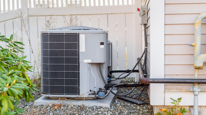 A home's outdoor AC unit with sticks and plants nearby