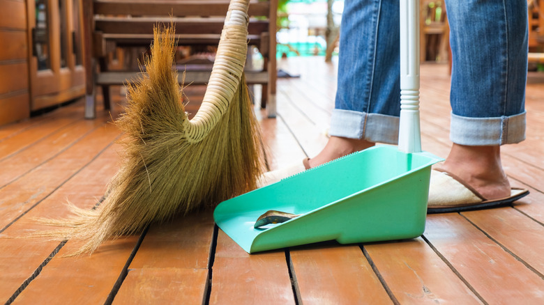 Person sweeping leaves off of their porch into a dustpan