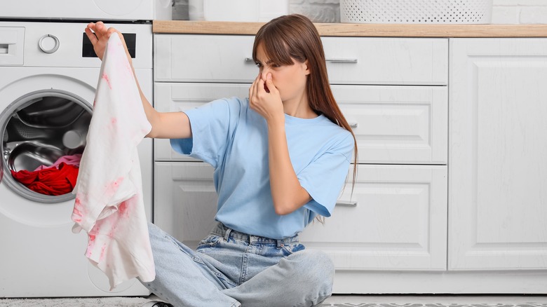 A woman holding up smelly clothes in laundry room