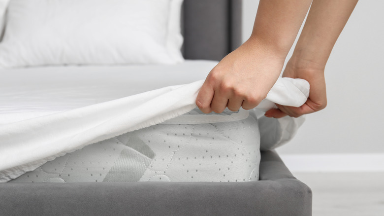 Hands pulling bed sheet cover over corner of mattress