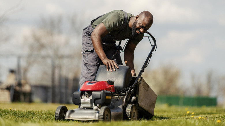 Man examining a lawn mower while working in yard