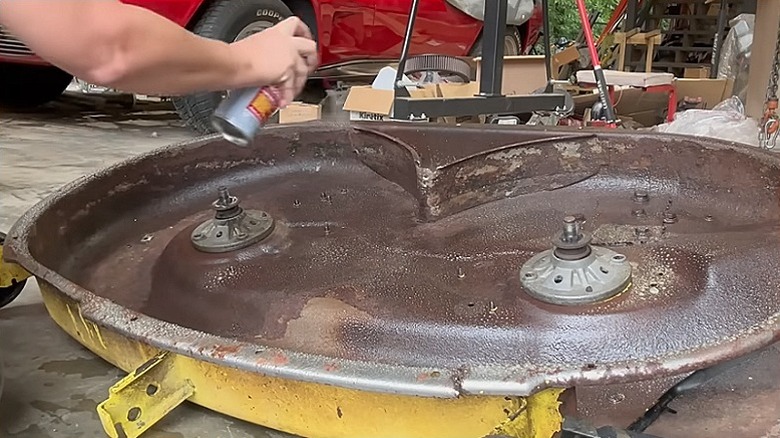 A person spraying the lawn mower deck with a rust preventative product