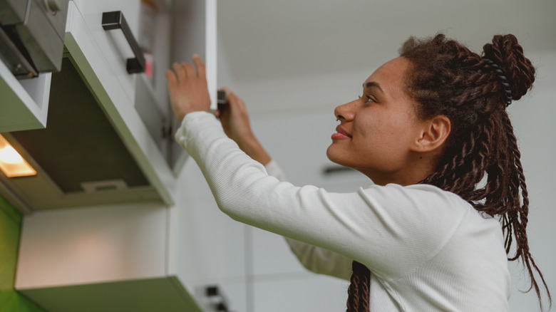 Woman opening upper kitchen cabinet door