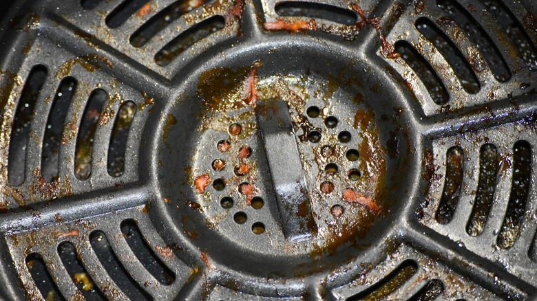 A close-up view of an air fryer tray with built-up grease and food particles