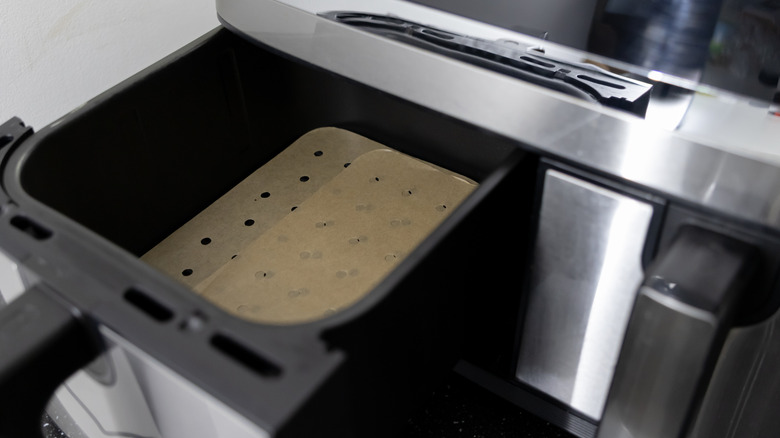 A close up of a clean air fryer with specialty parchment paper in the tray