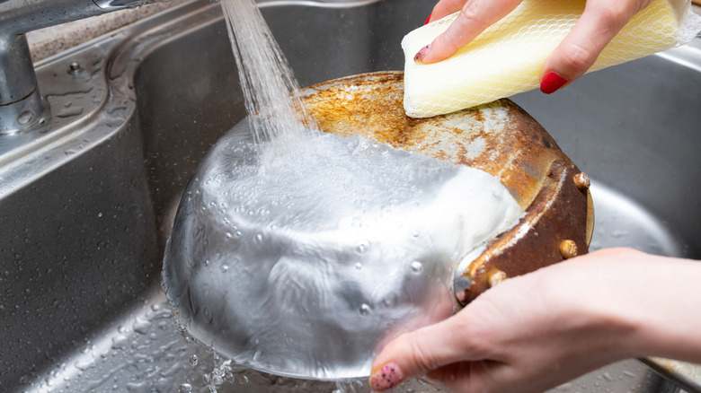 A person washing the bottom of a burnt frying pan with a sponge