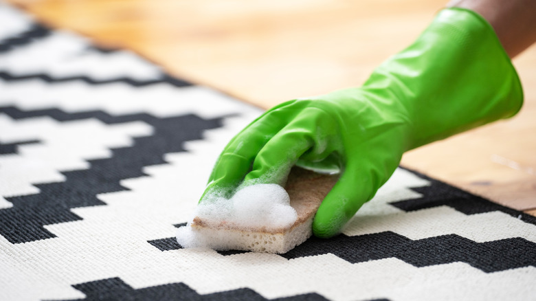 person cleaning rug with sponge