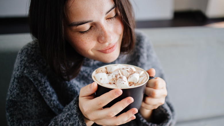 Woman in sweater drinking hot cocoa out of mug