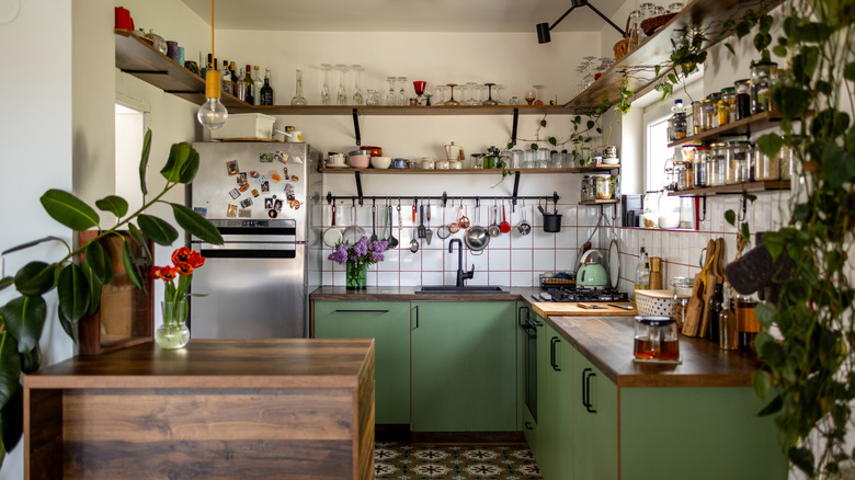 A cozy kitchen with green cabinets, open shelving and lots of plants