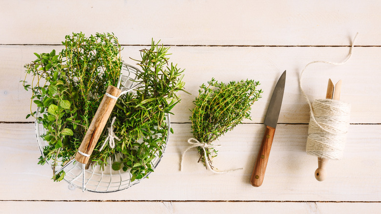 Fresh herbs next to a knife and string on wood planks
