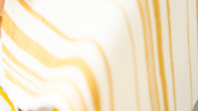 A close-up of someone sewing white and yellow striped fabric with a sewing machine.