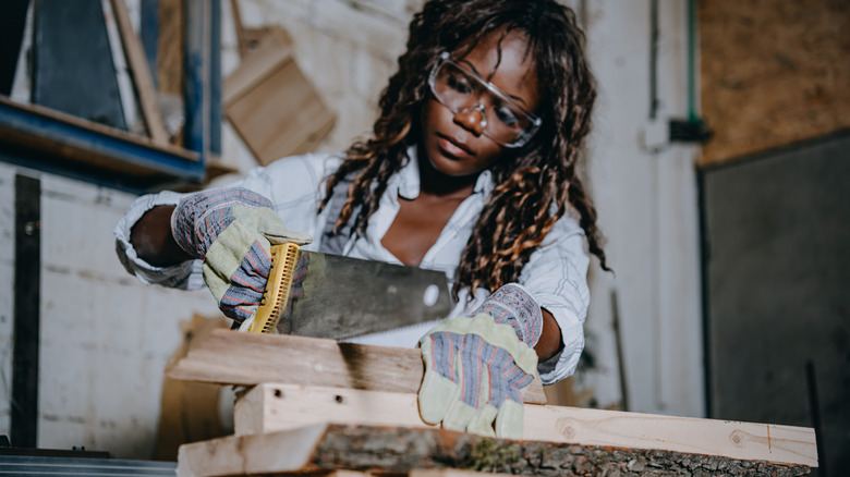 A woman using a saw to cut wood planks.