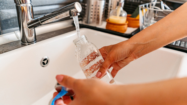 Person washing plastic water bottle in kitchen sink