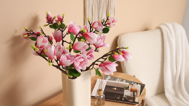 A vase of faux magnolias on a side table.