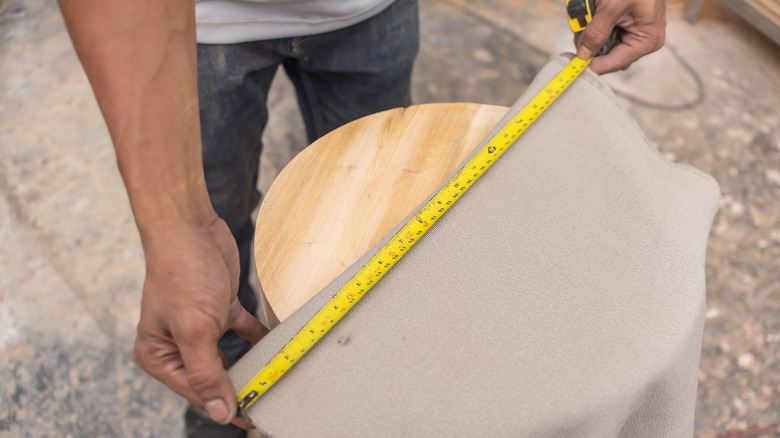 man measuring wooden stool 