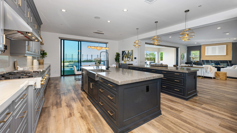 Kitchen with gray and black cabinets, stainless appliances, large islands, and sliding glass door in background.