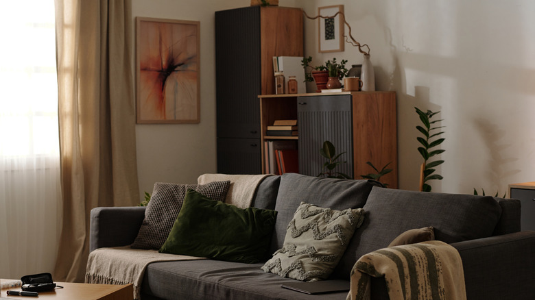 A warm greige room has orange-toned furniture and a gray couch.