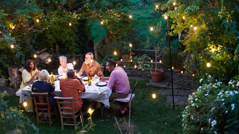 A group of people sit at an outdoor table in a cottagecore-inspired garden