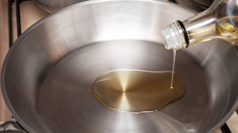 A person pours olive oil into a stainless steel pan on a stove