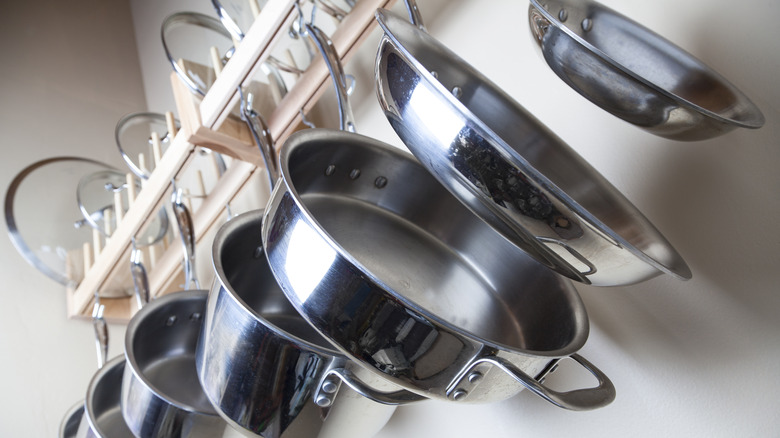 Stainless steel pans and their lids displayed on a kitchen wall storage rack