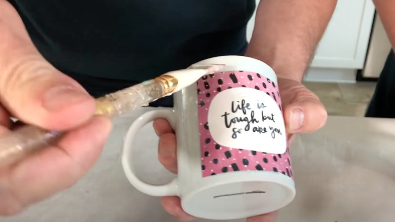 Person brushing clear Mod Podge onto DIY painted mug