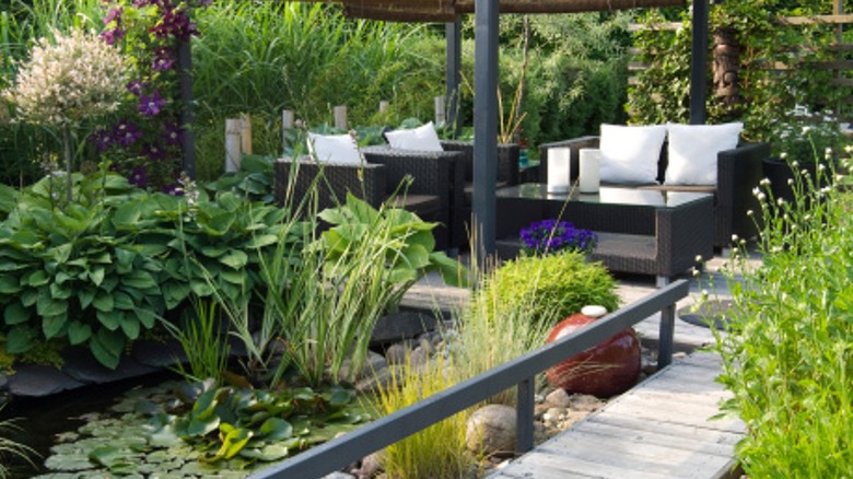 An outdoor patio with wooden pathways surrounding a pond with lots of greenery and modular furniture