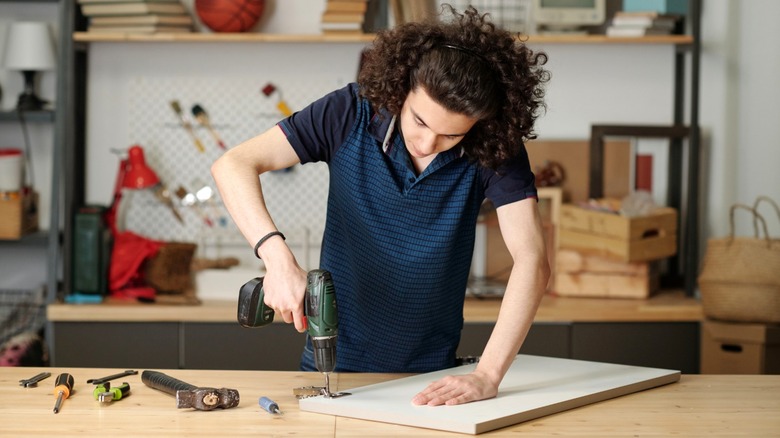 Person drilling screws into cabinet door hinges on workbench