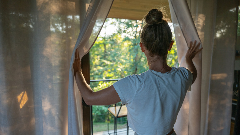 Person opening curtains at a sliding glass door, looking ahead at the patio.