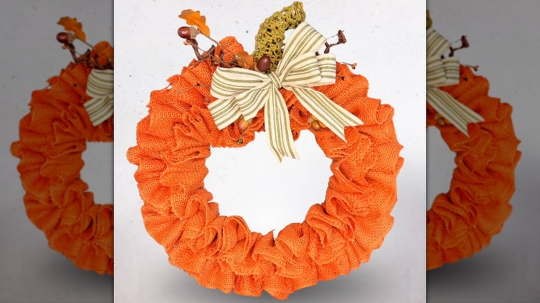 A fully decorated burlap ruffle pumpkin wreath with stem, bow, and fall embellishments.