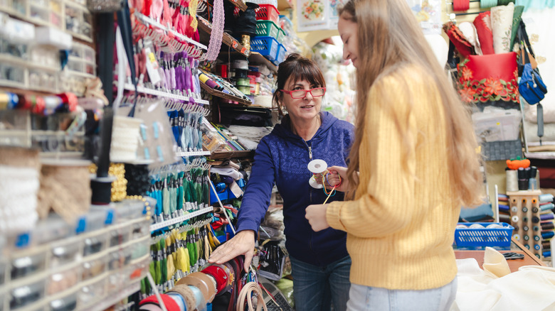 Woman shopping for fall craft supplies and employee showing her rolls of burlap.