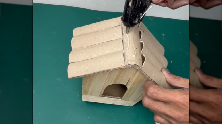 a person glues toilet paper rolls to the top of a cardboard diy bird house planter project