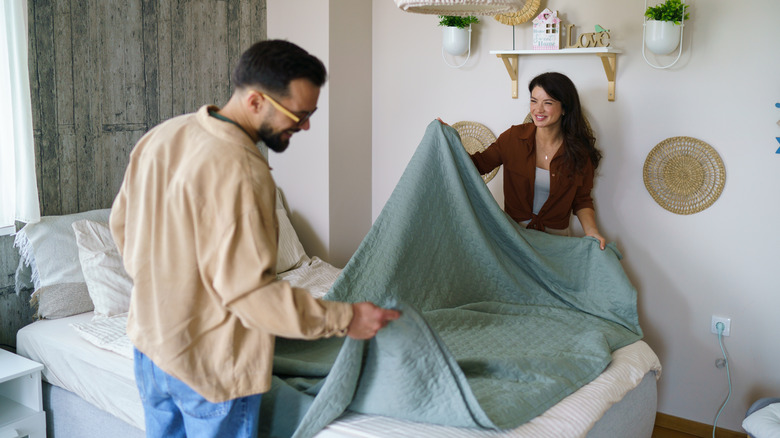 A couple smiling while making their bed