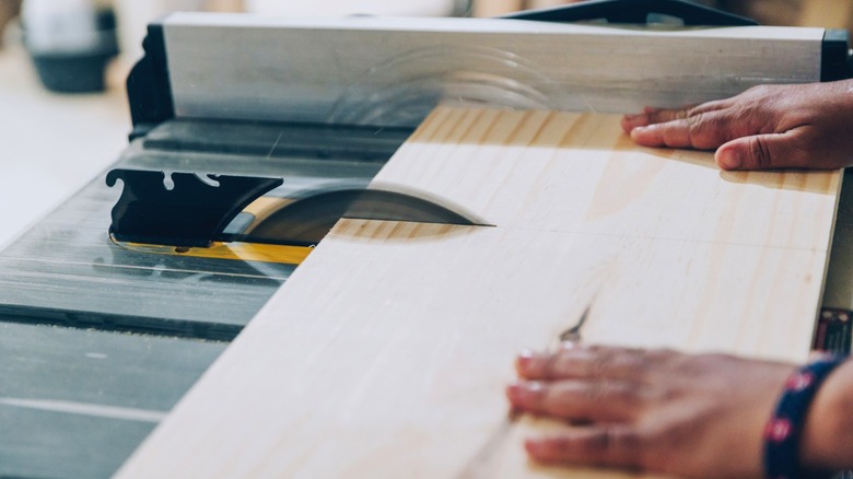 Person pushing wood board through table saw