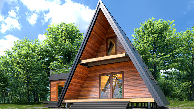 A-frame cabin clad in wood with deck and black roof with woods behind.