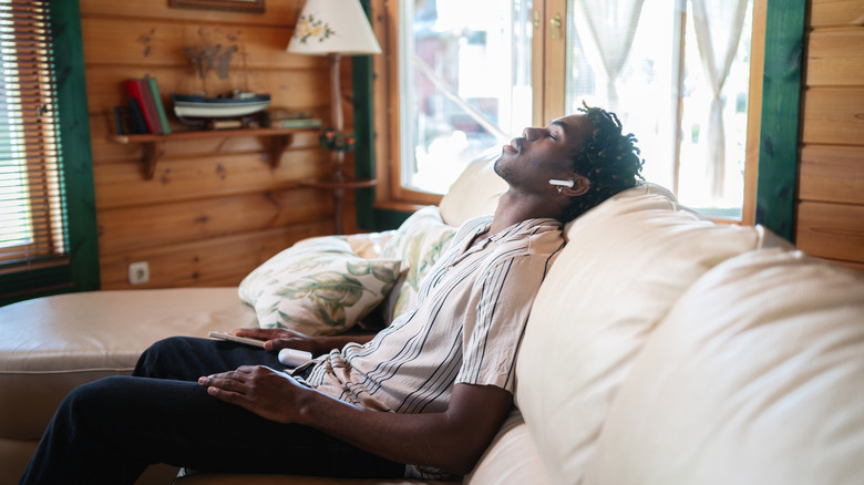 young man relaxing on an overstuffed counch in a wooden cabin