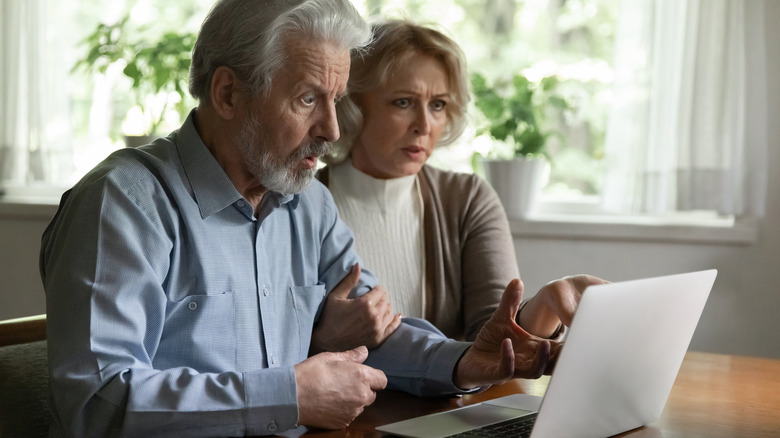 Elderly couple with shocked looks on their faces at a laptop problem