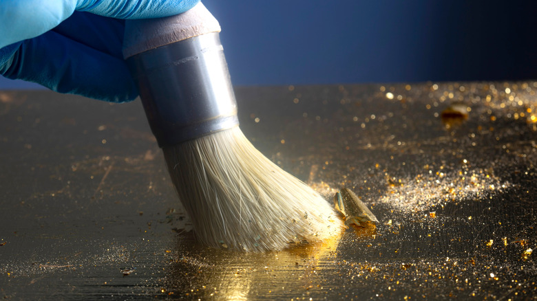 a brush glides across a metallic gold flaked surface