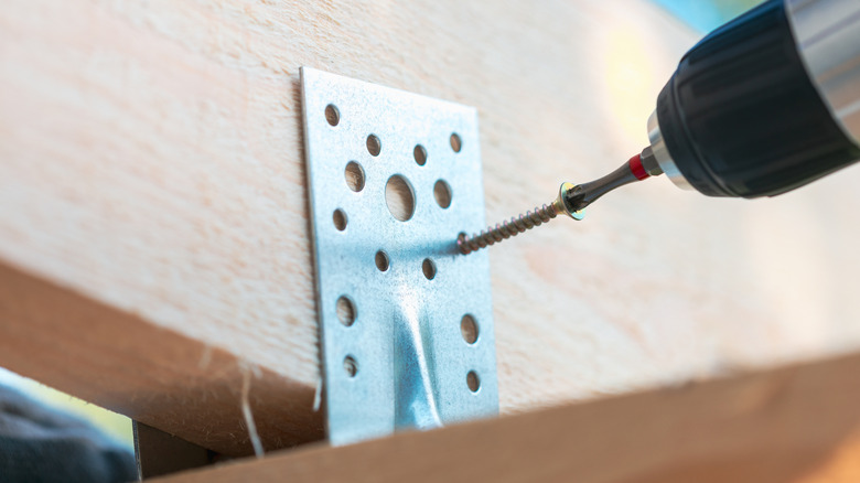 A closeup image of a screwdriver driving screw into metal bracket.