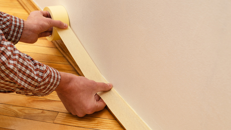 A man taping off a baseboard before painting
