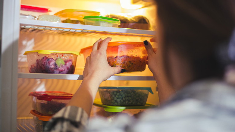 A person taking a container out of an open fridge