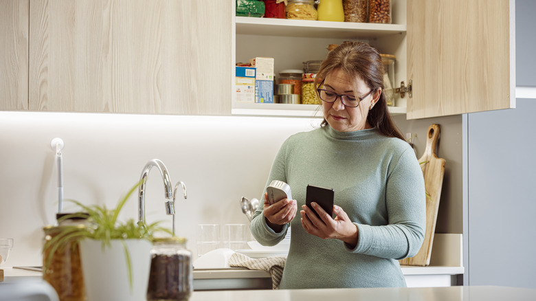 A woman looking at her phone and a can of food