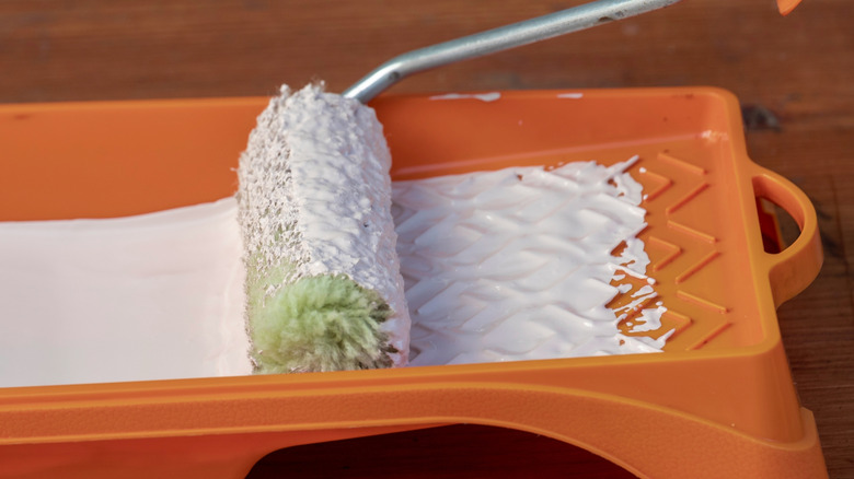 An orange paint tray filled with white paint with a large roller.