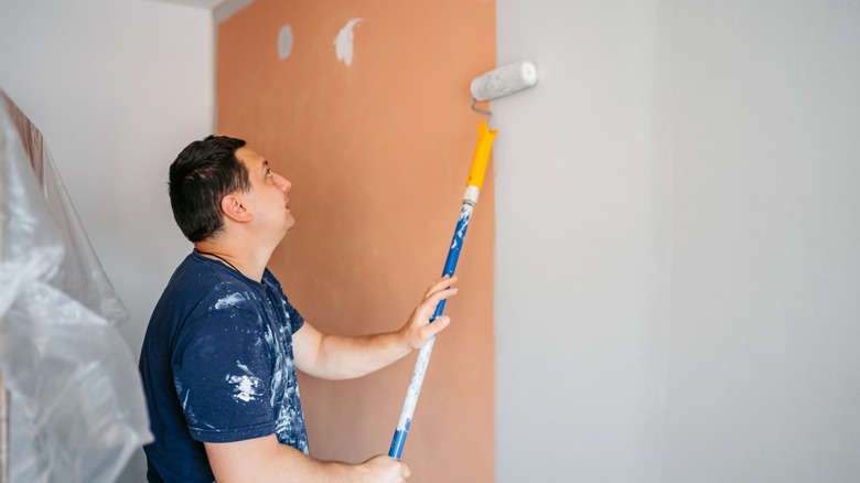 A man painting a wall with white paint on a long roller.