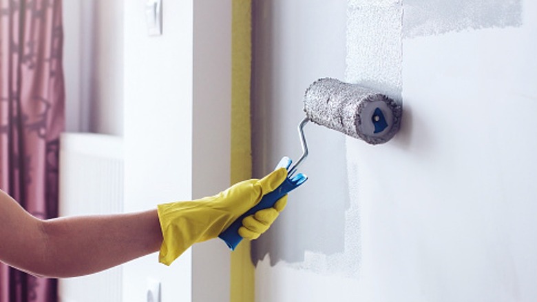 A gloved hand uses a roller to paint a wall.
