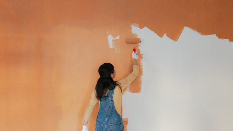 A woman painting her wall with orange paint