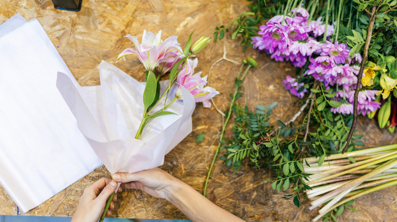 Hands working on a floral arrangement, the table laid out with various cut flowers and white paper