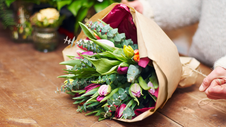 Person tying twine around a pink and green bouquet wrapped in brown craft paper