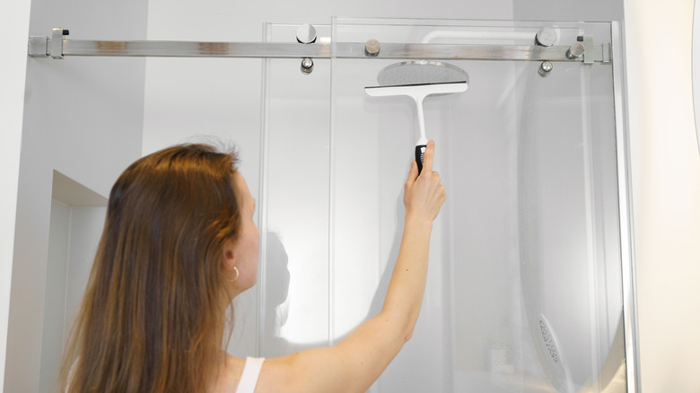 A woman cleans the glass door of her shower with a squeegee.