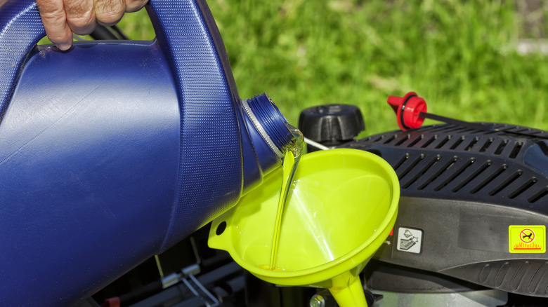 person pouring oil into lawn mower