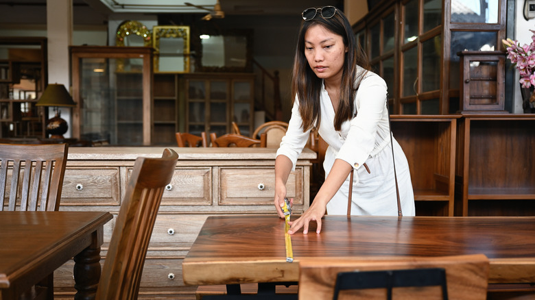A woman measuring a wooden table with a tape measure